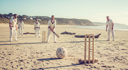 A cricket match unfolds on a beautiful sandy beach with players in action against a coastal backdrop bathed in sunlight.