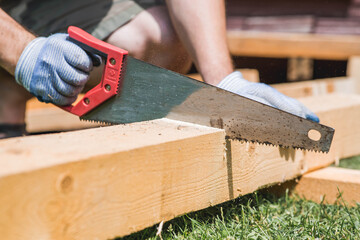A hand saw in the hands of a craftsman. A man sawing a beam with a tool. Production of wooden products. Construction, wood processing.