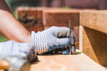 Close-up of a nail being driven into a board with a hammer. A carpenter wearing cloth protective...