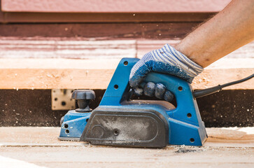 A hand-held electric planer in the hands of a craftsman. A man planing boards with an electric...