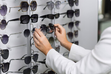 Close-up of hands of a young woman who chooses sunglasses on the showcase for purchase in an optical store. Optometry, eyesight, eyeglasses, accessories, fashion, lifestyle