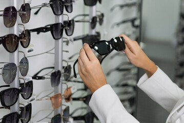 Close-up of hands of a young woman who chooses sunglasses on the showcase for purchase in an optical store. Optometry, eyesight, eyeglasses, accessories, fashion, lifestyle