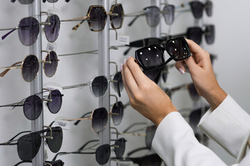 Close-up of hands of a young woman who chooses sunglasses on the showcase for purchase in an optical store. Optometry, eyesight, eyeglasses, accessories, fashion, lifestyle