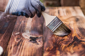 The procedure for protecting and coating wooden boards. A worker applies a protective wood stain...