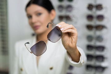 Close-up of the hands of an elegant young brunette woman who holds sunglasses in an optical store. Choosing eyeglasses to buy, vision, protection, lifestyle, fashion