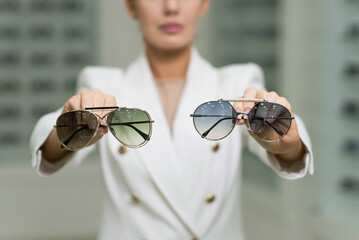 Close-up of the hands of an elegant young brunette woman who holds sunglasses in an optical store. Choosing eyeglasses to buy, vision, protection, lifestyle, fashion
