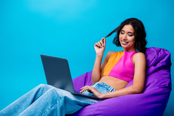 Young woman enjoying leisure time on a bean bag with a laptop, wearing colorful casual attire...