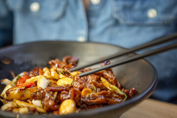 Close-up of spicy stir-fried beef with garlic, chili peppers, and vegetables in a glossy sauce, served in a black bowl with chopsticks. Bold and flavorful Asian cuisine.