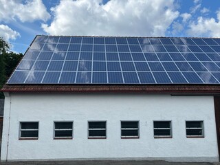 Fototapeta premium Solar cells on an old roof, blue sky with white clouds in the background, concept: renewable energies