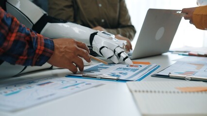 A close-up view of a collaborative workspace showcasing a human hand and a robotic arm working together on data analysis, highlighting modern technology.Noogenesis