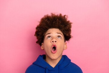 Fashionable boy with a surprised expression wearing a blue hoodie standing against a vibrant pink...