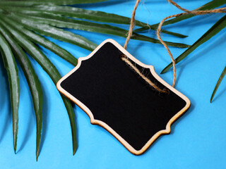 Wooden black price tag and palm leaves on blue background.