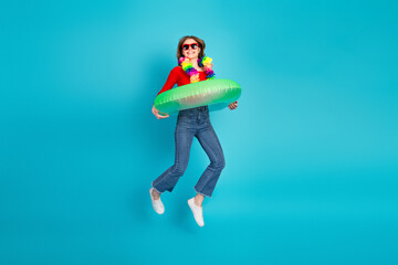 Young woman with colorful lei and float ring standing against a blue backdrop in casual jeans and...