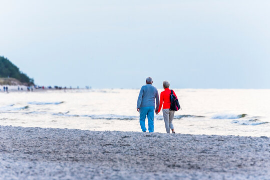 Elderly couple walking hand in hand on a sandy beach near the Baltic Sea. 
