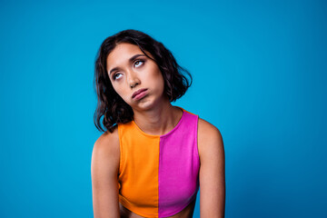 Attractive young woman making an expressive eye roll pose against a solid blue background in a...