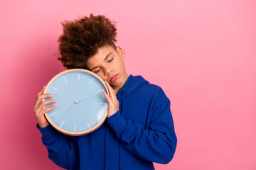 Young boy in blue hoodie holding clock against vibrant pink background expressing time and...