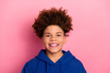 Happy teenage boy smiling joyfully in blue hoodie against bright pink background showcasing style...