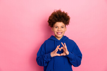 Cute child showing love gesture with hands clad in blue hoodie against a cheerful pink background