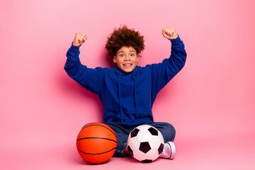 Excited young boy celebrating with sports equipment against a bright pink background