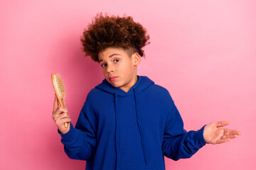 Young boy in a blue hoodie holds a hairbrush against a pink background, displaying a casual and...