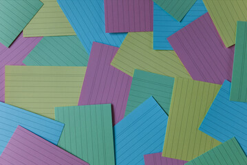 Colorful lined index cards are scattered across a surface, creating a vibrant and organized pattern. Multicolor background with flash cards. Working and studying supplies and stationery.