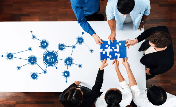 Aerial view of a diverse group collaborating on a business strategy, assembling puzzle pieces while discussing digital graphics for innovative solutions. Amity - Powered by Adobe