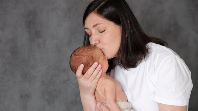 Mother gently kisses forehead of newborn baby boy in arms