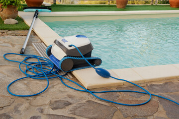 At the pool with clean turquoise water, there is a cleaning robot and a pool cleaning brush. The concept of cleaning pools in hotels, resorts and country houses.