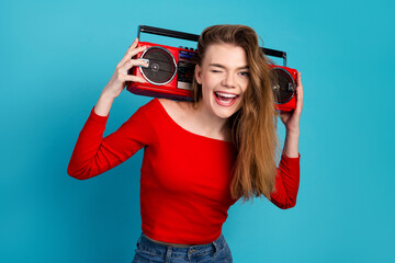 Cheerful young woman posing with a red retro cassette player against a bright blue background and...