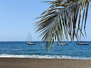 view of a black sand beach in Guadeloupe in the French Antilles with sailboats on the Caribbean Sea on a sunny day

