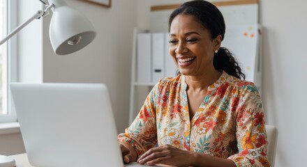 A happy woman smiles while working on her laptop in a bright and clean home office setting.
