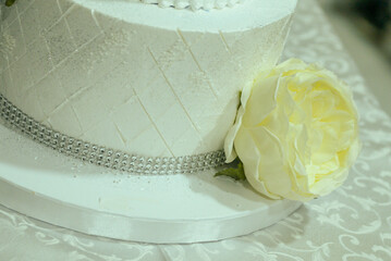 A two-tiered blue and white birthday cake decorated with a pearl ribbon and white and yellow flowers with the female name Ana written in Cyrillic script