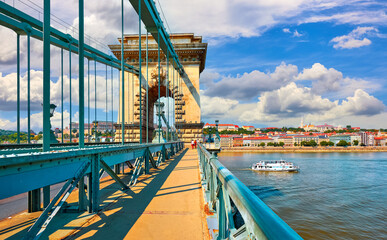 Chain bridge in Budapest, Hungary. Touristic travel boat on Danube river. Antique lanterns street lamps along road and stone arcs. Summe urban landscape with blue sky and clouds.