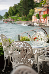 Beautiful cafe with empty chairs on Varenna waterfront on a sunny summer afternoon shoot during windy cloudy day, Lake Como, Lombardy, Italy