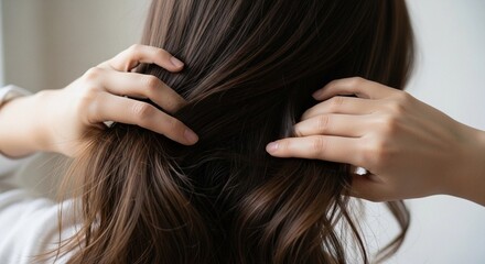 Fototapeta premium Hands gently comb through long, wavy, brown hair, capturing a serene moment. The shiny strands reflect natural light, suggesting health and vitality. Hands are delicately posed