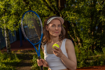 Young woman with tennis racket and ball, wearing sporty white outfit on outdoor court