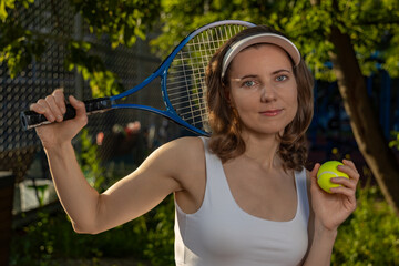 Young woman with tennis racket on shoulder, holding ball, wearing sporty white outfit