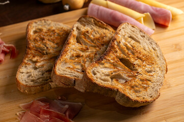 Healthy, organic, whole and sliced ​​homemade sourdough bread with ham and cheese on a wooden table and kitchen utensils with an airy crumb and crispy crust. 