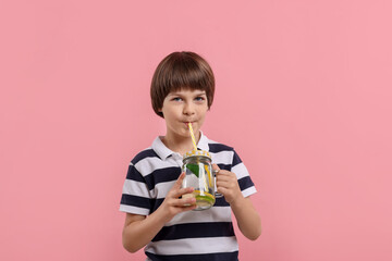 Cute little boy drinking lemonade on pink background. Refreshing drink
