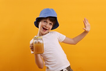 Happy little boy in panama hat with mason jar of juice on orange background. Refreshing drink