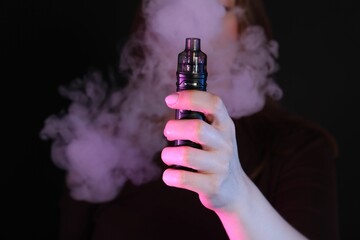 Woman using electronic smoking device in neon lights on black background, closeup