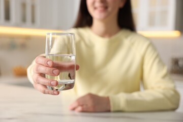 Woman with glass of water at table in kitchen, selective focus