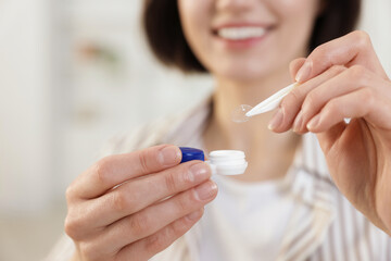 Woman taking contact lens out of case indoors, closeup