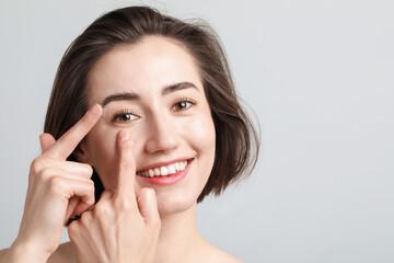 Woman putting in contact lens on light background. Space for text