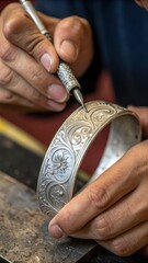 A close-up of a silversmith’s hands engraving intricate patterns into a silver bracelet