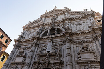 The magnificent marble facade of a historic Venetian church, rich with statues and sculptural details, seen from a low angle