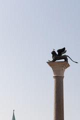  A minimalist view of the famous Lion of Saint Mark column in Venice, with a seagull perched on top. The clear sky provides ample copy space