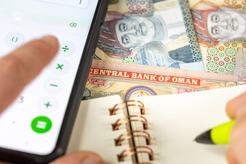 Oman rial, Counting on smartphone calculator, OMR money, notes in notebook. Financial settlement,...