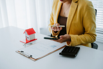 Smiling real estate agent calculating mortgage and presenting house model while sitting at her desk...