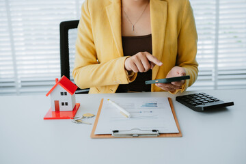 Smiling real estate agent calculating mortgage and presenting house model while sitting at her desk...